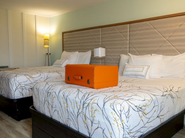 A neatly made hotel bed with patterned covers and pillows, with an orange suitcase placed on top in the center.