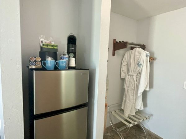 A small room with a mini fridge and coffee items on the left, and a white bathrobe hanging on a stand on the right.