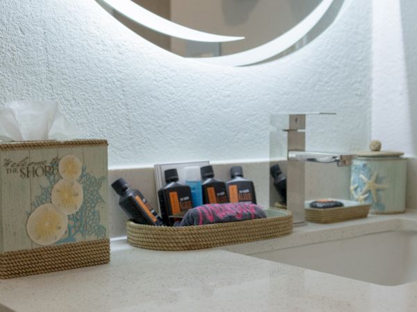 A bathroom counter with wicker baskets holding assorted skincare bottles and towels, styled with a beach theme.