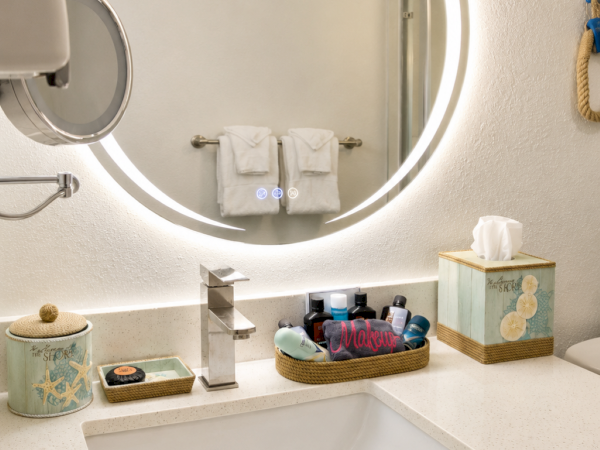 A modern bathroom sink with a glowing round mirror, folded towels, and neatly arranged toiletries on the counter.
