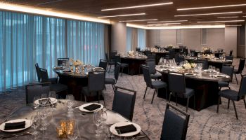 The image shows an elegantly set dining room with round tables, black chairs, and ambient lighting, ready for an event or banquet.