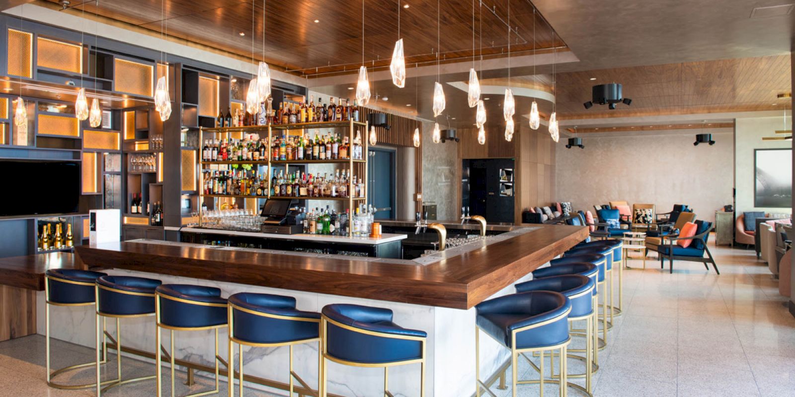 A modern bar with blue stools, pendant lights, and a well-stocked back bar in a stylish lounge setting.