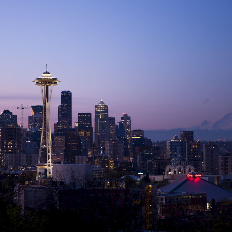 Seattle skyline at dusk featuring the Space Needle, city buildings, and Mount Rainier in the background under a twilight sky.