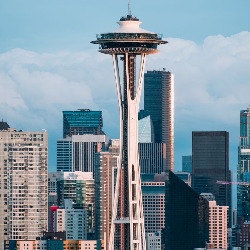 The image features the Space Needle with a backdrop of modern skyscrapers and a cloudy sky in the Seattle skyline.