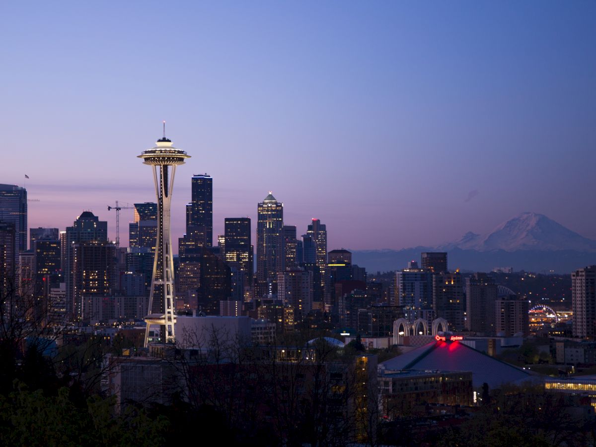 A nighttime cityscape with illuminated buildings and a backdrop of mountains, featuring a prominent tower with a disk-shaped top.